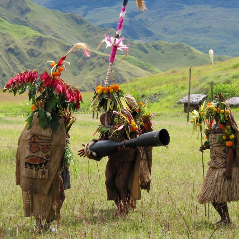 Highland dancers in feathered headdresses crossing a grassy valley
