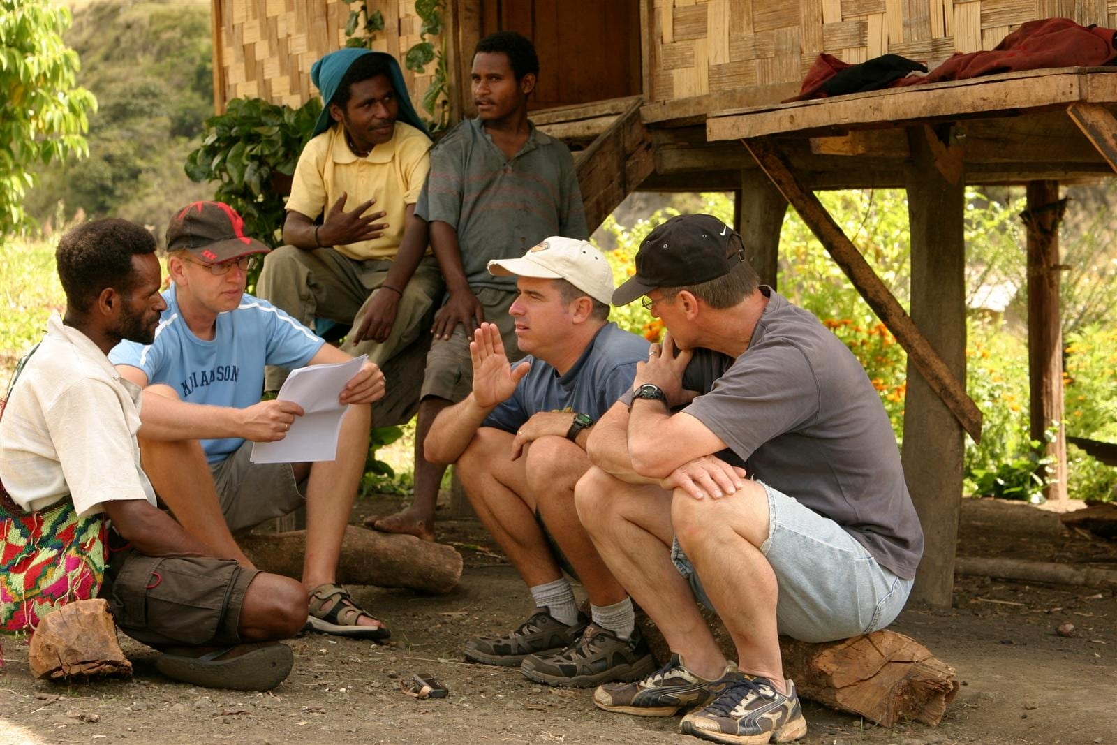 Missionaries in conversation with local men outside a stilted house